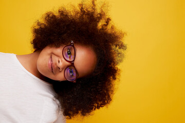 portrait of a young African girl in glasses smiling and rejoicing on a clean yellow background