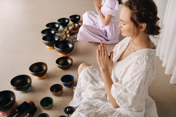 Two women are sitting with Tibetan bowls in the lotus position before a yoga class in the gym