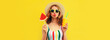 Leinwandbild Motiv Summer colorful portrait of beautiful young woman blowing her lips with cup of juice and lollipop or ice cream shaped slice of watermelon wearing straw hat on yellow background, blank copy space