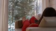 © ShantiMedia - A woman in red is lying on a sofa with a smartphone in her hands in front of a window in which trees are visible. The virtual world on the Internet does not allow you to see the real world.