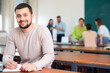© JackF - Portrait of positive man student sitting at table and handwriting during lesson in university.