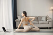 © prostooleh - Woman doing yoga while watching online workout tutorials on laptop at home