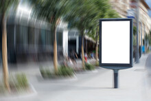 White Blank Vertical Billboard In The City. Sidewalk With Benches, Trees And Townspeople. Rotation Blur. Mock-up.