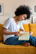 © Daniel - Young African American woman reading a book sitting on yellow couch. Female relaxing at home. Vertical image.