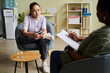 © Seventyfour - Teenage girl sitting on armchair and listening to advice of psychologist while she making notes on paper during session at office