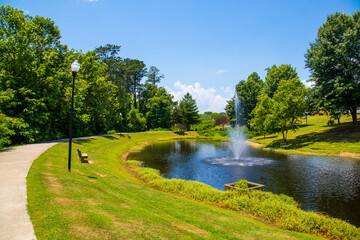 Wall Mural - a gorgeous summer landscape in the park with a pond with a water fountain surrounded by lush green trees, grass and plants with blue sky and clouds at Logan Farm Park in Acworth Georgia USA