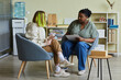 Leinwandbild Motiv African female social worker talking to difficult teenage girl while they sitting on armchairs at office