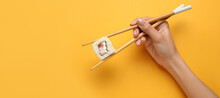 Hand Holding Chopsticks With Delicious Sushi Roll On Yellow Background With Space For Text