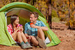 © Maridav - Camping couple drinking water in tent smiling happy outdoors in forest enjoying sun at looking at view. Happy multiracial couple relaxing after outdoor activity hiking. Asian woman, Caucasian man