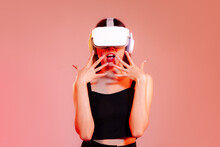 Metaverse Concept, Young Asian Woman In Black Tank Top Wearing Vr Headset Posing Exciting On The Red Pastel Screen Background.