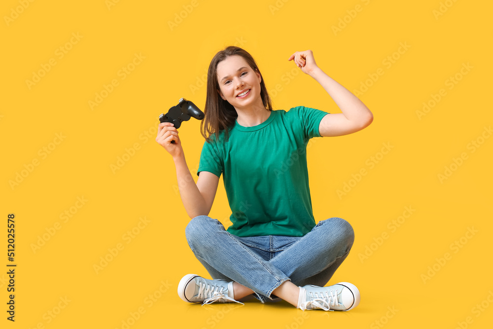 Pretty young woman with game pad sitting on yellow background
