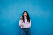 © Westend61 - Smiling young beautiful woman showing number one with index finger in front of blue wall