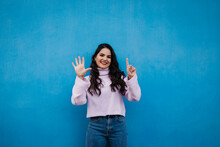 Smiling Young Beautiful Woman Showing Number 6 In Front Of Blue Wall