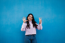 Smiling Young Beautiful Woman Showing Number 8 In Front Of Blue Wall