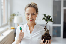 Smiling Businesswoman Holding Plant Showing Green Thumb In Office