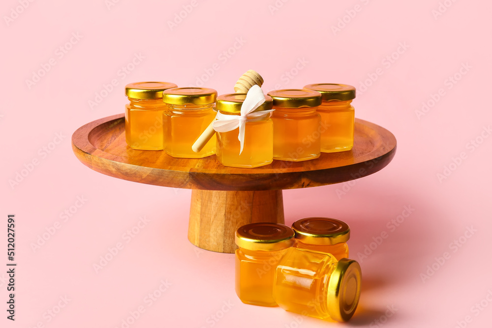 Dessert stand with jars of honey on pink background