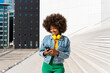 © Westend61 - Smiling Afro woman text messaging through smart phone standing by steps on sunny day
