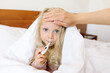 © Westend61 - Sick girl measuring body temperature wrapped in blanket