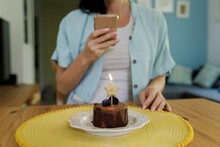 Woman Photographing Birthday Cake With Burning Star Shape Candle Through Mobile Phone