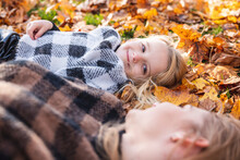 Smiling Girl Looking At Mother Lying On Autumn Leaves In Park