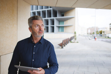 Businessman holding tablet PC standing by wall