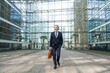 © Westend61 - Businessman with bag walking in front of modern glass building
