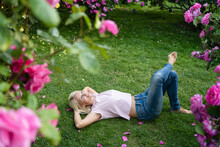Thoughtful Woman With Hands Behind Head Lying On Grass At Rose Garden