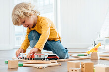 Cute Boy With Blond Hair Playing With Toy Train Set At Home