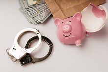 Bribe And Financial Fraud Concept. Envelope With Dollars, Broken Piggy Bank And Handcuffs On A Table Close-up