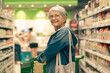 Portrait smiling senior woman making purchases in the supermarket pushing shopping cart. Caucasian elderly customer in grocery store