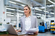 © Westend61 - Smiling businesswoman with laptop and documents in factory