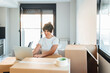 © Westend61 - Woman using laptop on cardboard box at new home