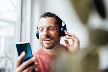 Smiling Man With Headphones Using Smart Phone At Home