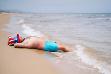 Carefree Shirtless Man Wearing Uncle Sam Hat Relaxing Near Seashore At Beach