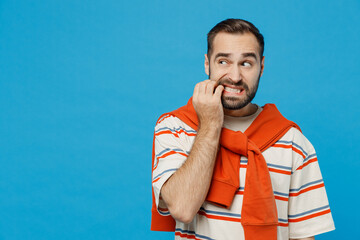 Wall Mural - Young sad mistaken puzzled worried confused caucasian man 20s in orange striped t-shirt looking aside biting nails fingers isolated on plain blue background studio portrait. People lifestyle concept.