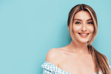 Closeup portrait of young beautiful smiling female in trendy summer clothes. Carefree woman posing near blue wall in studio. Sexy positive model having fun indoors. Cheerful and happy. Isolated