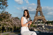 happy young woman in stylish outfit using smartphone while sitting near eiffel tower in paris.