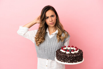 Wall Mural - Young woman holding birthday cake over isolated pink background having doubts