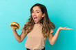 © luismolinero - Young woman holding a burger over isolated background with shocked facial expression