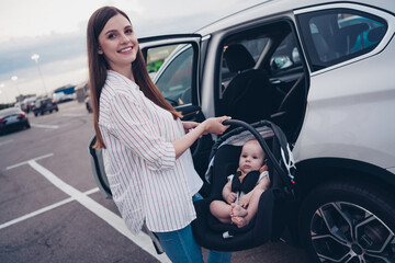 Wall Mural - Photo of pretty charming mommy little son dressed casual clothes putting car seat inside auto transport open door