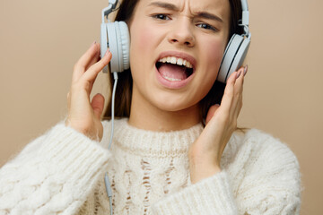 Wall Mural - close horizontal photo of a woman in a white sweater listening to music in her wired headphones smiling broadly with happiness and holding them with her hands while looking at the camera with delight