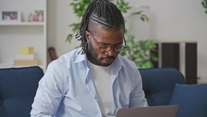 Black programmer in eyeglasses working on laptop at home, freelance job