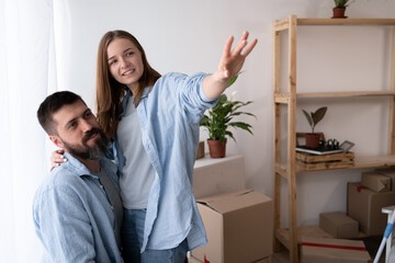 Happy couple hugging moving new house sitting on the box, spouses portrait, people in living room on relocation day smiling looking