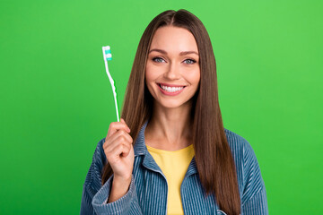 Wall Mural - Portrait of cheerful charming lady hand hold toothbrush beaming smile isolated on green color background