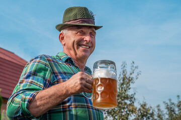 Senior men with beer mugs with Bavarian beer in Tyrolean hats celebrating a beer festival in Germany. Happy old people during the October holiday in Munich