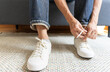 © bennnn - Man tie the shoelace of white sneakers sit on wood bench at home.