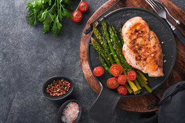 Wall Mural - Chicken breast grilled with vegetables. Grilled chicken steak, asparagus and cherry tomatoes in black plate on gray concrete table background. Healthy diet lunch. Barbecue steak fried. Top view.