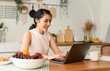 © NaMong Productions - Beautiful young asian woman working on laptop computer while sitting at the kitchen room background.