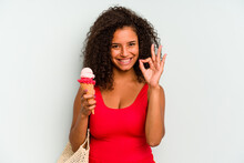 Young Brazilian Woman Going To The Beach Holding An Ice Cream Isolated On Blue Background Cheerful And Confident Showing Ok Gesture.