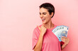 © Asier - Young caucasian woman holding banknotes isolated on pink background points with thumb finger away, laughing and carefree.